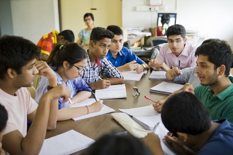 A group of students working round a table in the classroom while a teacher observes.