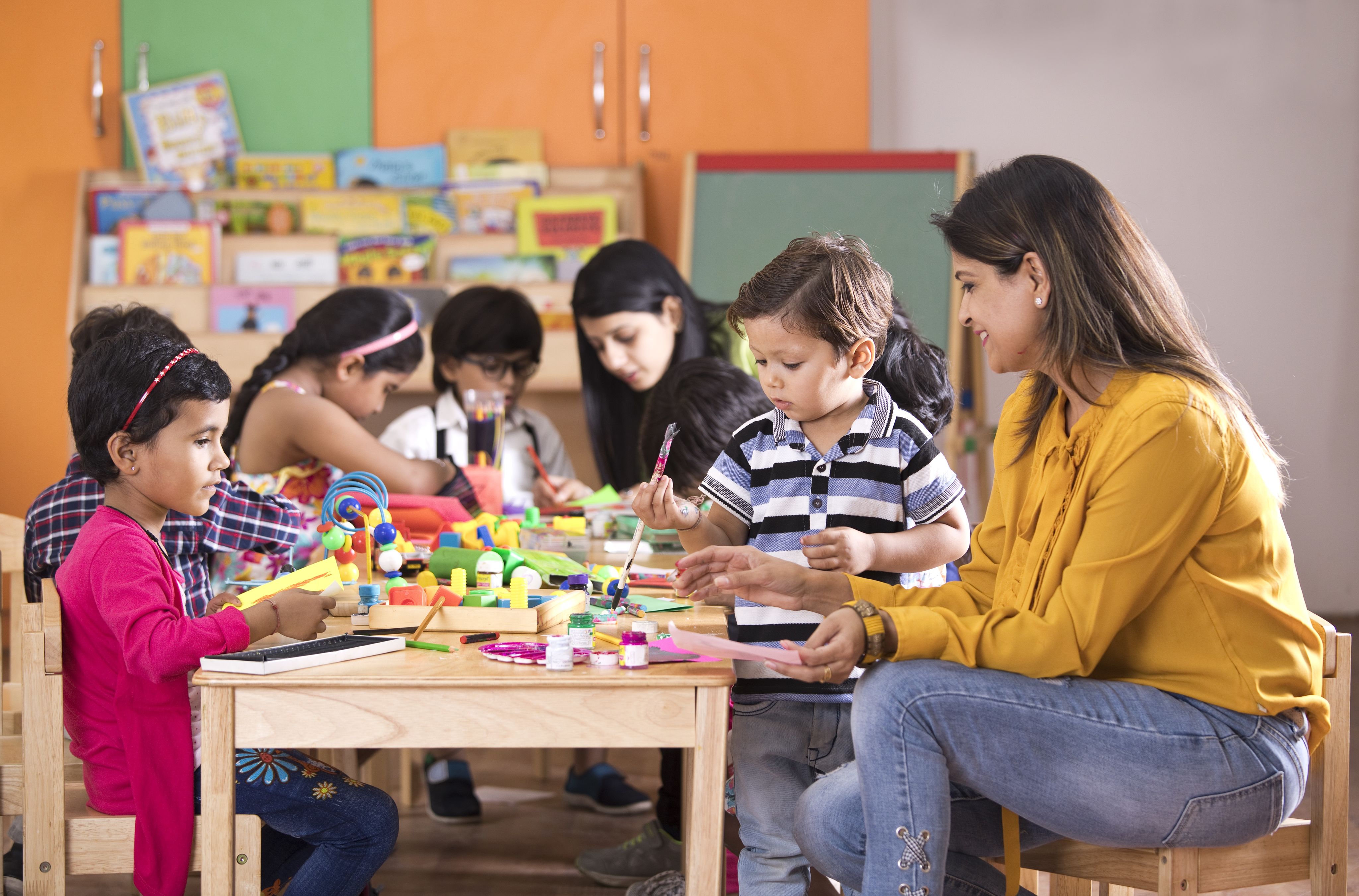 Teacher and children sitting at a table doing some painting and craft