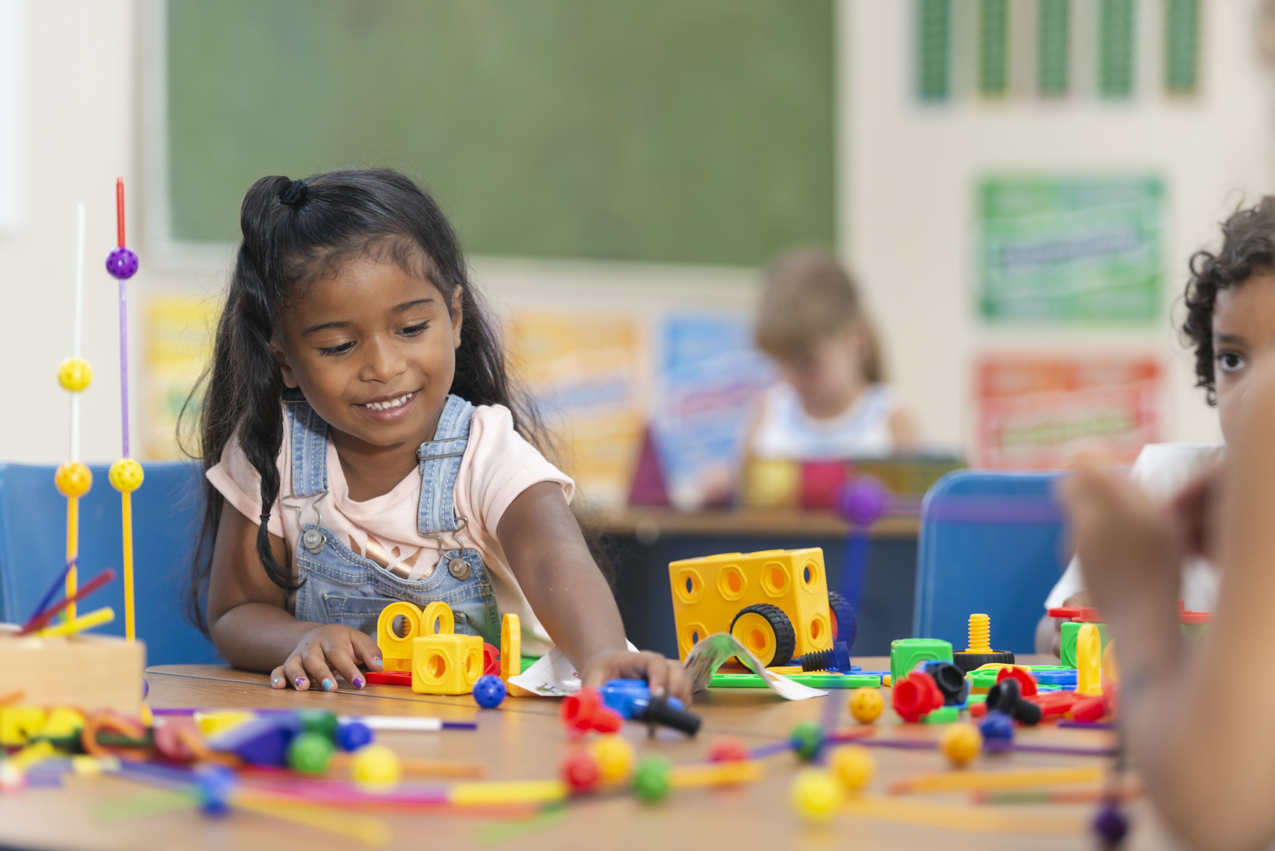 Girl playing with brightly coloured toys at a table. Smiling.