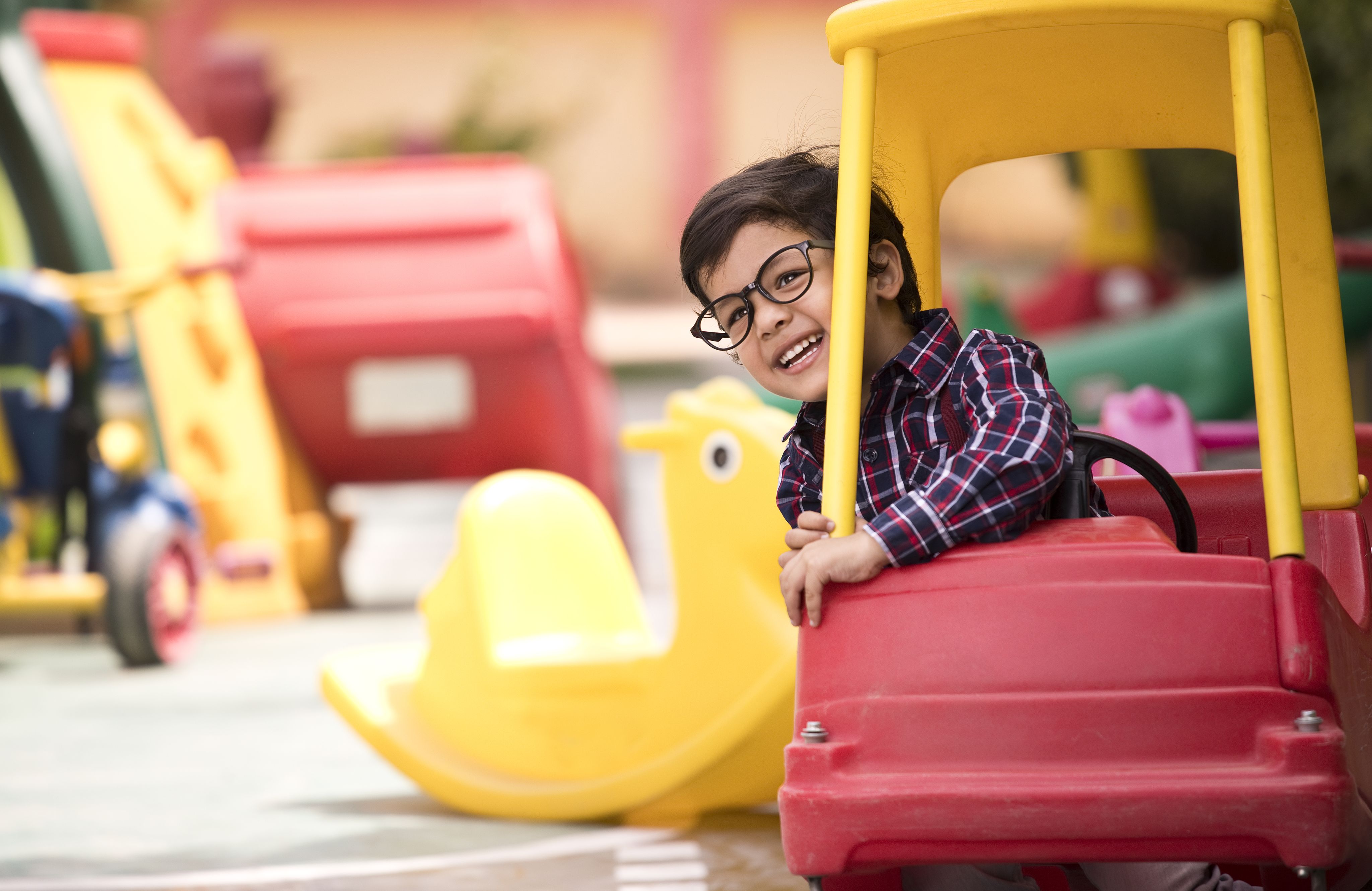 Boy with glasses smiling, sitting in a toy car in playground