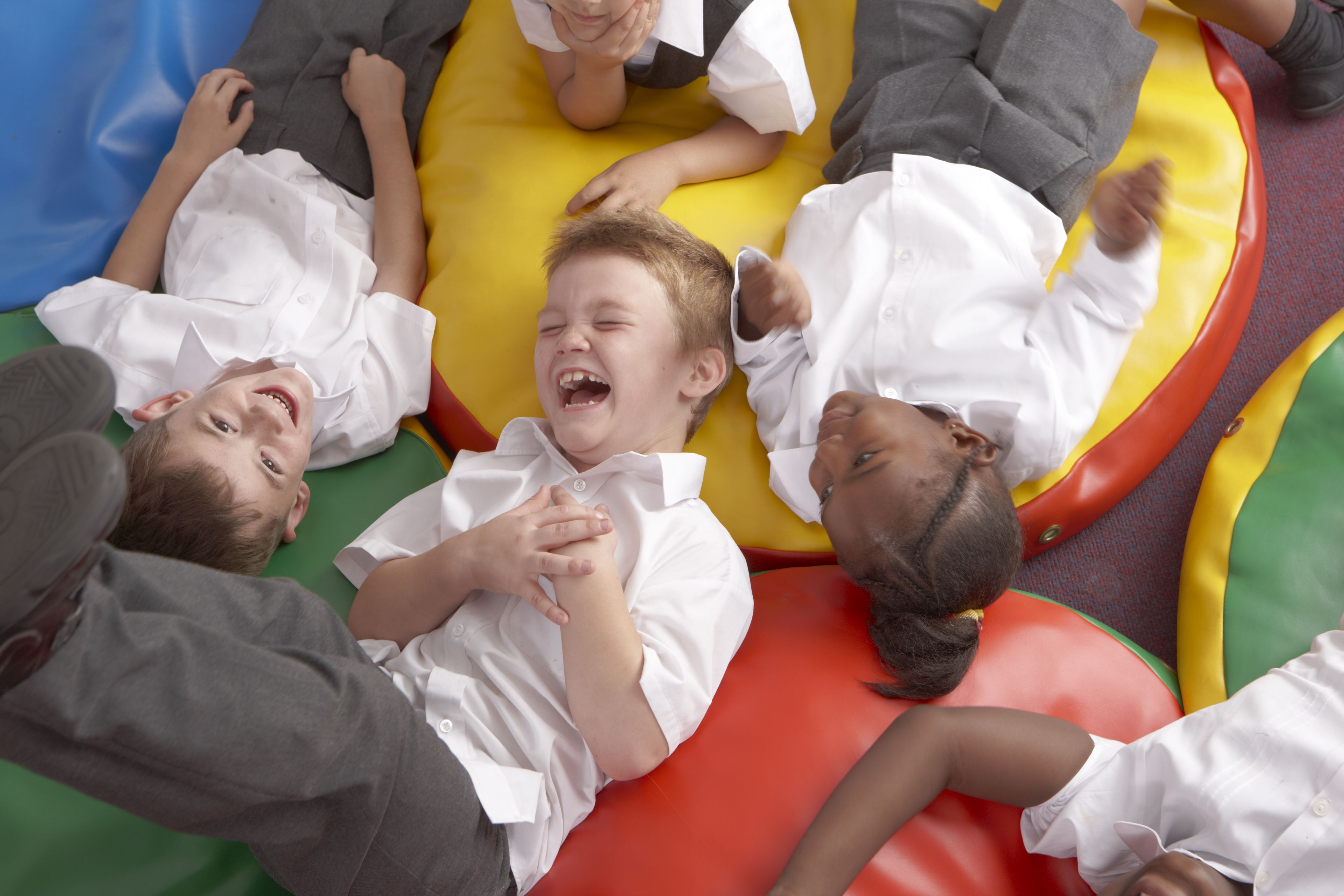 Group of multi-ethnic children laying on soft, colourful cushions laughing