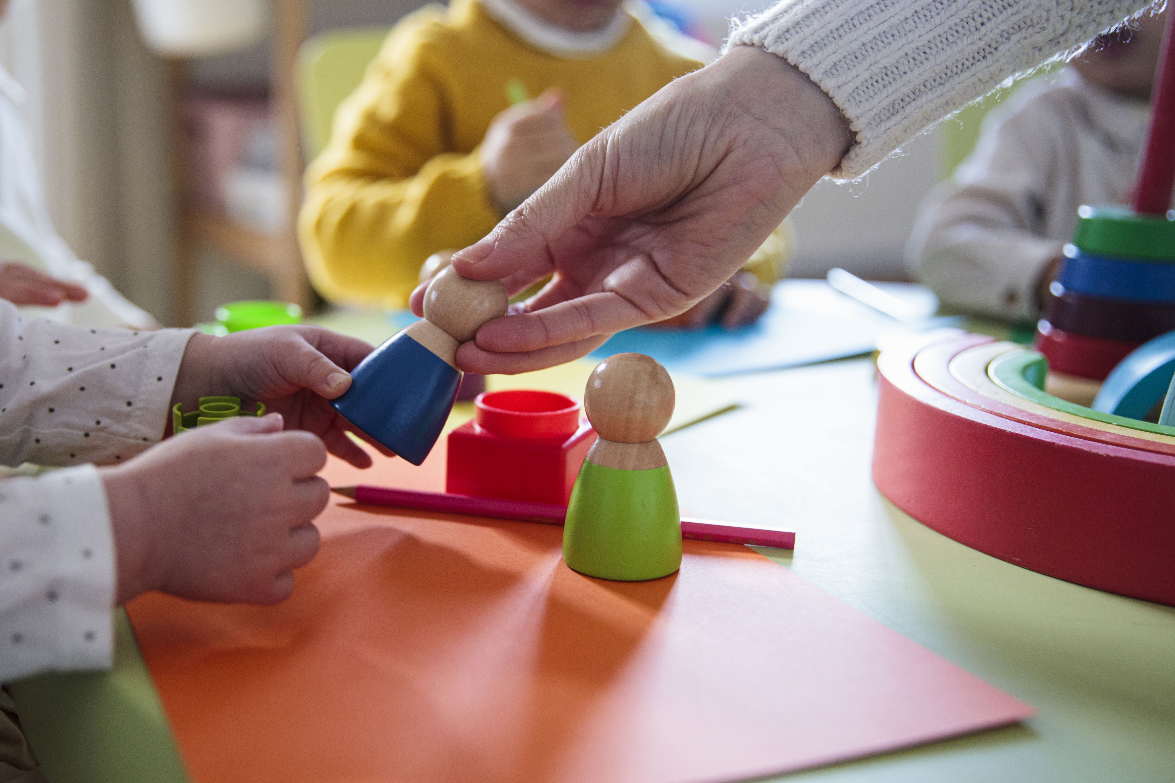 Adult hand moving a small wooden toy towards a child's hand