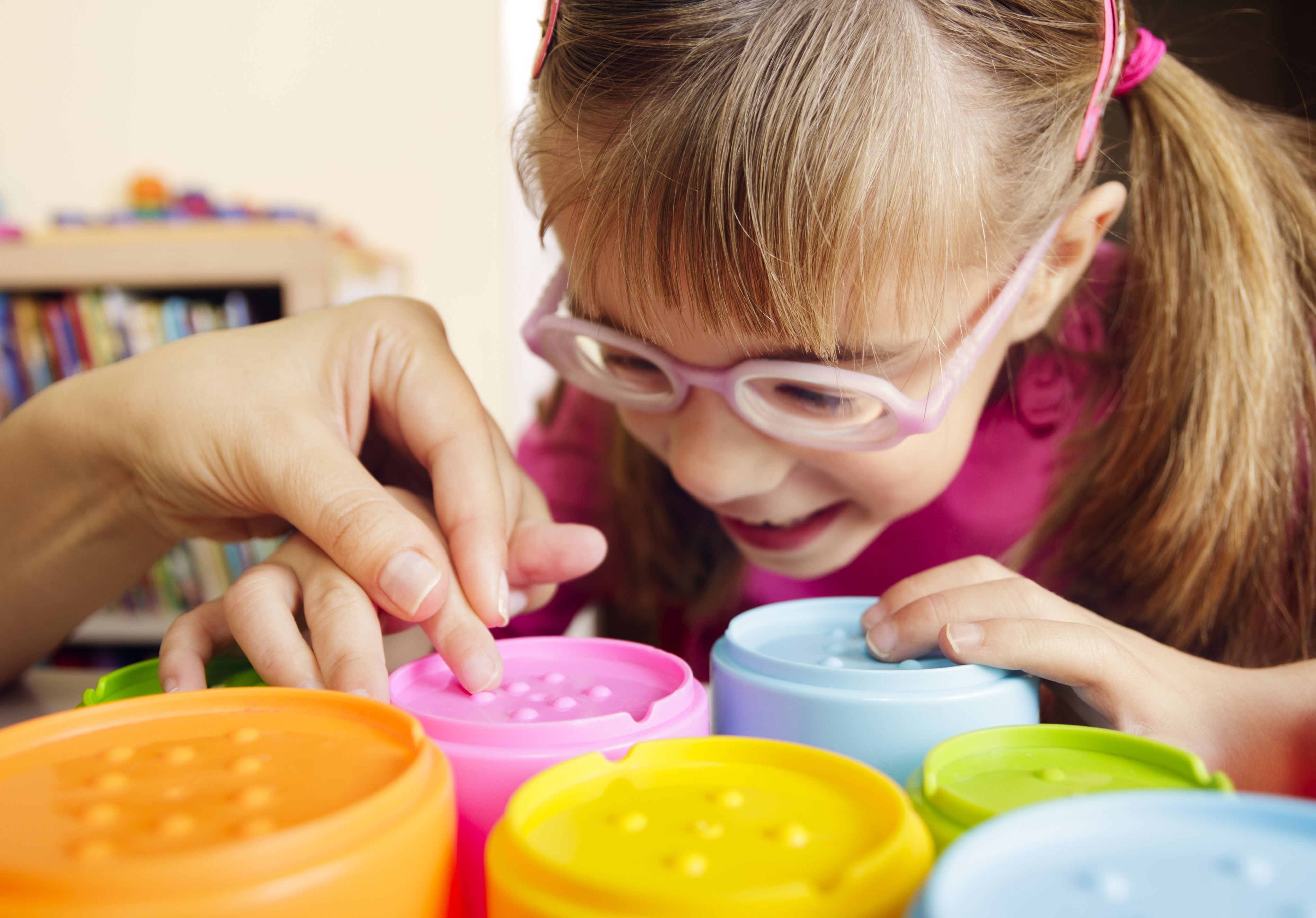 Girl with glasses touching bumps on coloured cups with adult hand holding her hand